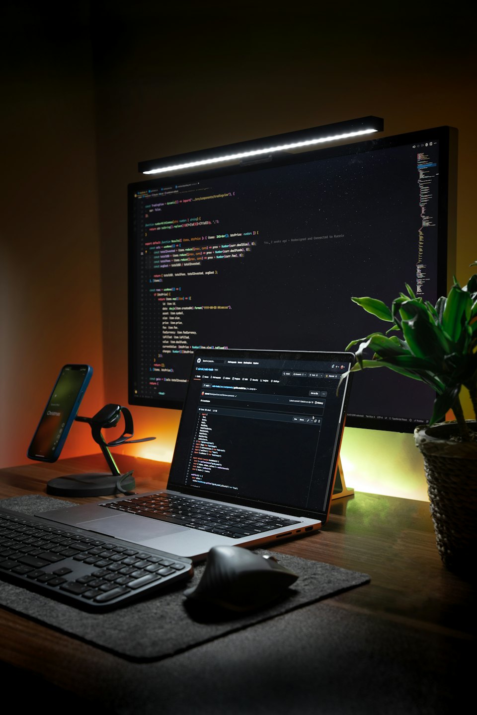 Biurko programisty z laptopem, monitorem, telefonem i rośliną.